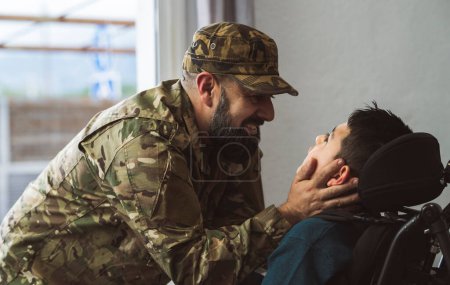 Téléchargez les photos : Hispanic veteran soldier caresses disabled son in a wheelchair when returning from military service to home . Unconditional love and inclusion concept. Focus on father face - en image libre de droit