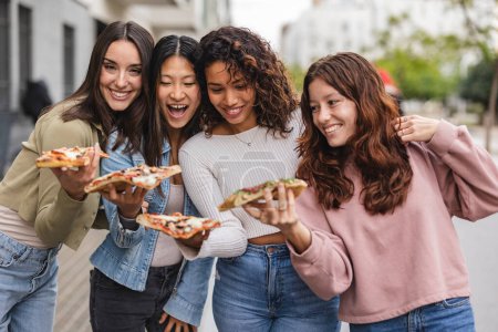 Téléchargez les photos : Amis féminins multiraciaux manger de la pizza dans la ville - en image libre de droit