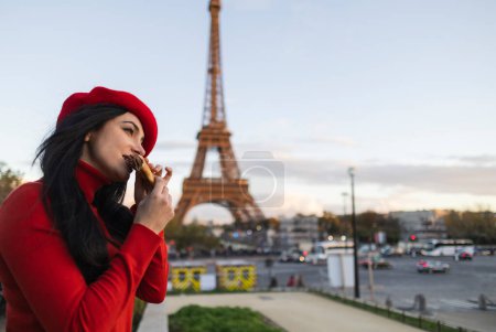Téléchargez les photos : Une touriste à la mode portant un béret rouge prend une photo selfie avec la Tour Eiffel en arrière-plan à Paris, en France. manger une crêpe parisienne typique, voyage conceptuel. - en image libre de droit
