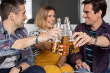 Group of cheerful friends clinking beer bottles in a toast while enjoying a casual get-together.