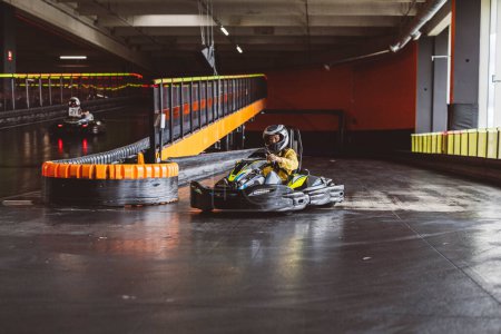 Fahrer im gelben Anzug biegt scharf auf Indoor-Kartbahn ab.