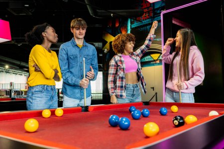 Group of young adults concentrated in a lively game of billiards.