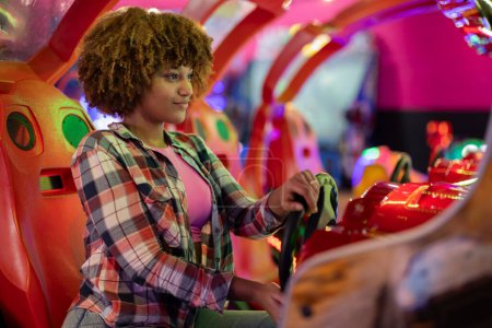 Young woman with curly hair deeply engaged in playing a space-themed arcade machine.
