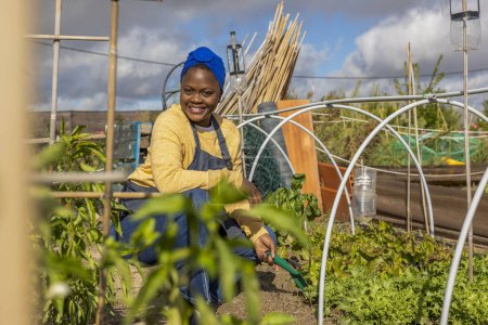 A beaming young woman tends to her garden plot, surrounded by an abundance of fresh greens.