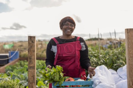 A joyful mature woman showcasing fresh produce from her community garden plot.