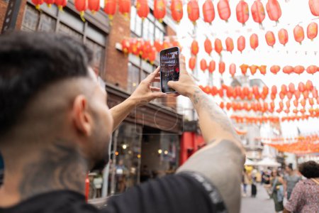 Man taking photo of vibrant street lanterns with phone.