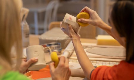 Téléchargez les photos : Mains soigneusement mouler l'argile jaune sur une pièce de poterie, soulignant l'art détaillé de la céramique. - en image libre de droit
