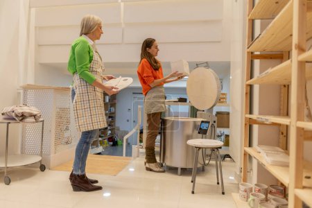 Teamwork im Einsatz als Seniorin und erwachsene Frau, die den Ofenbetrieb in einem Töpferatelier leitet und sich dabei auf das Handwerk konzentriert.