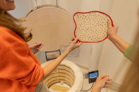 Two artisans showcase a hand-painted polka-dotted ceramic plate before kiln firing.