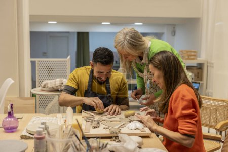 A senior artisan, a man, and a woman engage in a collaborative clay crafting session in a pottery class.