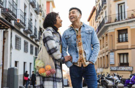 Jeune couple portant un sac d'épicerie ensemble dans une rue urbaine animée.
