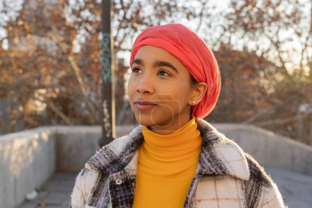 An inspiring stroll through the city, a woman in a pink headscarf walks with grace, embodying the spirit of a cancer fighter.