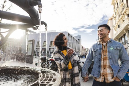 A joyful couple shares a laugh near a city fountain, basking in the urban environment.