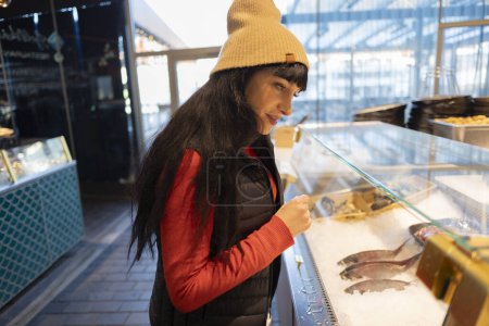 A joyful woman interacts with a seafood display at an indoor market.