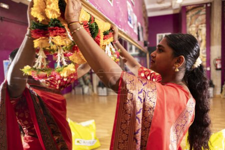 Una mujer india en un sari montando una guirnalda floral.