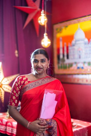 A radiantly smiling Indian woman stands before a brightly colored festive backdrop.