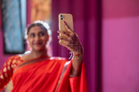Eine junge Inderin hält ihr traditionell geschmücktes Spiegelbild mit einem Smartphone fest.