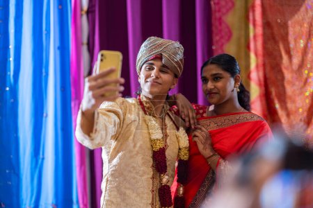 Vibrant and joyful, a young Indian woman captures her elegance in a red saree with a smartphone selfie.