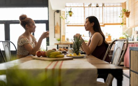 Eine herzerwärmende Szene, in der zwei junge Frauen ein fröhliches Gespräch während eines gesunden Frühstücks in einer gemütlichen Küche führen.