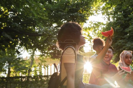 Une femme sourit en appréciant la pastèque avec des amis dans le cadre d'un coucher de soleil radieux dans le parc.