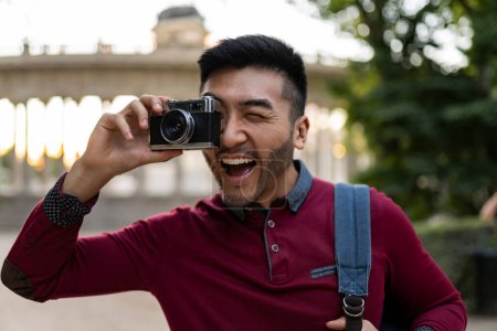 Das Lachen eines Mannes spiegelt die Freude am Fotografieren wider, als er mit seiner Oldtimer-Kamera im Park wegklickt.