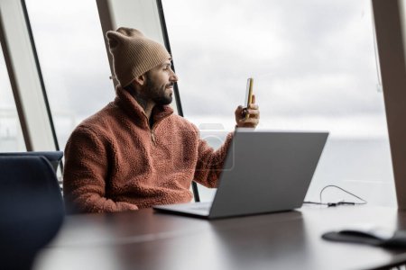 Ein nachdenklicher Mann hält am Fenster eines modernen Arbeitsplatzes inne, um Ideen auf seinen Notizblock zu notieren.