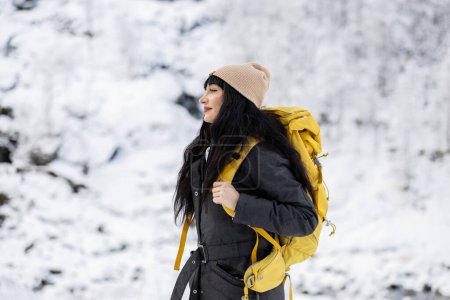 A woman in winter attire with a bright backpack enjoys a hike in the snowy landscape.