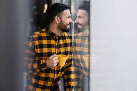 A man enjoys a moment of reflection with his coffee, as his smile is mirrored in the bus station glass.