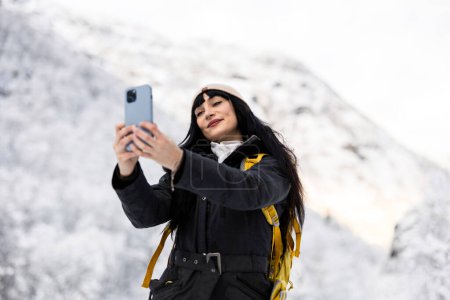 A female adventurer takes a selfie amidst a breathtaking snowy mountainous backdrop.