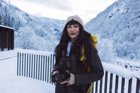 Porträt einer lächelnden Fotografin, die ihre Kamera hält und bereit ist, die winterliche Schönheit um sich herum einzufangen.