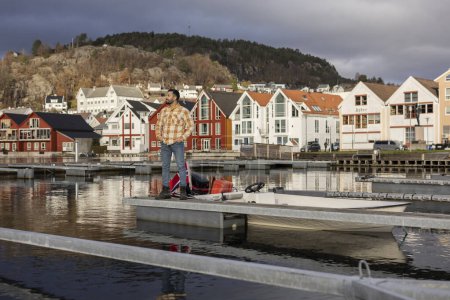 A male in his 30s prepares for a boating adventure against a backdrop of colorful Norwegian houses.