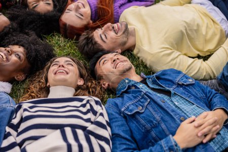 Foto de Un círculo cercano de jóvenes amigos se acuestan en la hierba, compartiendo alegría en un sincero momento de risa y relajación. - Imagen libre de derechos