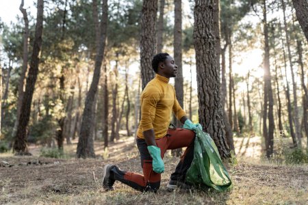 Arrodillado, este excursionista comprometido recoge basura, mostrando su dedicación a preservar el estado prístino del bosque.