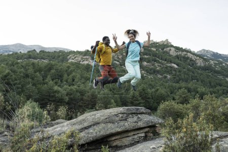 Hochstimmung in Höhenlagen: Ein Paar springt überschwänglich auf einen Felsvorsprung, den Blick auf die Berge hinter sich..