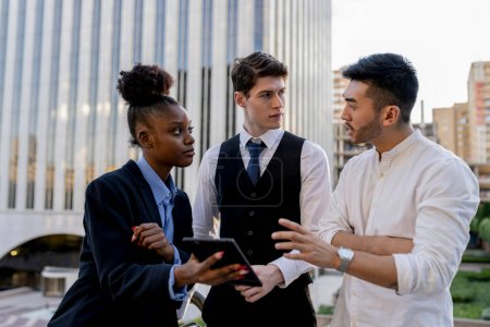 Three young, diverse professionals engaged in a serious discussion, using a digital tablet to navigate complex challenges at a city business district.