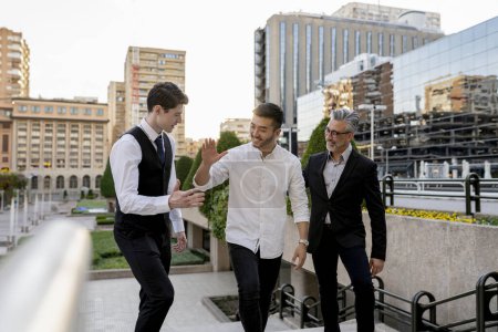 Un grupo diverso de profesionales de negocios que dan un chequeo en un entorno urbano al aire libre, simbolizando una exitosa colaboración en equipo.