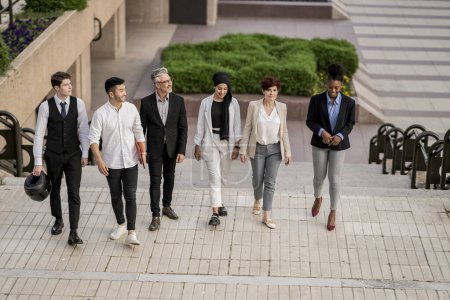 A diverse group of six business professionals confidently walking together through a city landscape, symbolizing teamwork and unity in a corporate environment.
