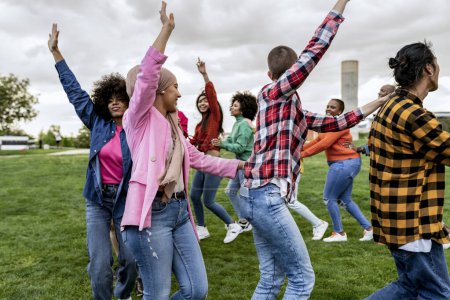 A vibrant group of young adults express their joy and unity by dancing and raising their hands in the air, celebrating a moment together outdoors.