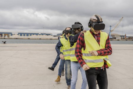 Téléchargez les photos : Les travailleurs de la construction s'engagent de manière ludique dans une simulation de réalité virtuelle, améliorant le travail d'équipe dans un port industriel. - en image libre de droit