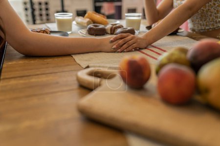 Concéntrese en las manos de dos personas que conectan sobre una mesa de desayuno, simbolizando la amistad y el apoyo, rodeado de una comida saludable.
