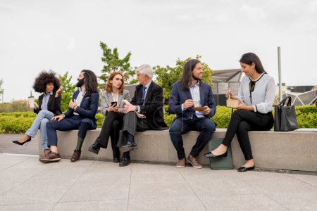 Professional group from various backgrounds discussing business strategies while enjoying a coffee break on a city plaza, reflecting a relaxed yet productive work culture.