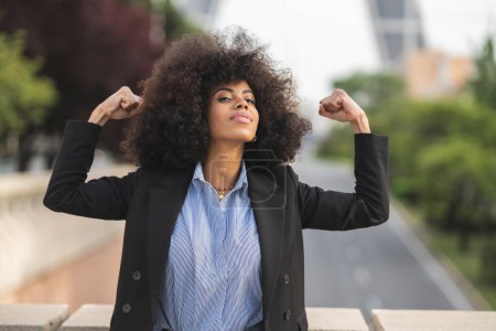 Empresaria afroamericana confiada alzando los puños en la victoria, mostrando empoderamiento y éxito en un contexto urbano.