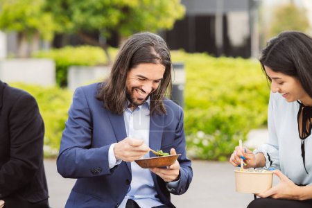 Felices compañeros de trabajo compartiendo una risa durante un almuerzo al aire libre, comidas saludables en la mano.