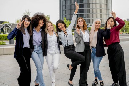 Group of vibrant female professionals in joyful poses, celebrating teamwork in an urban setting.