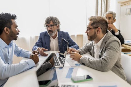 Un groupe diversifié de professionnels masculins s'engagent dans une discussion approfondie sur les stratégies d'entreprise, en se concentrant sur les données numériques dans un environnement de bureau bien éclairé.
