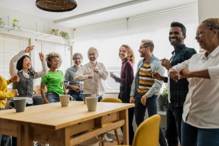 A diverse office team enjoys a lively celebration, dancing and sharing moments of joy in their well-lit, plant-filled workspace.
