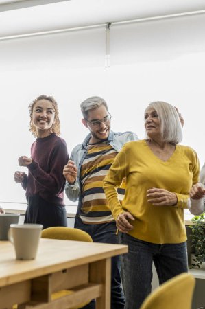 Colleagues of different ages and backgrounds share a playful dance moment, celebrating team spirit and diversity in a sunny office environment.