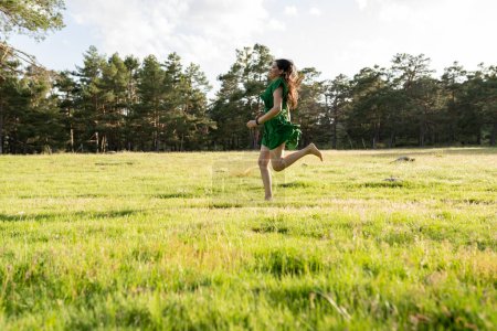 A young woman in a vibrant green dress runs barefoot across a lush field, her hair flowing in the wind, embodying freedom and joy.