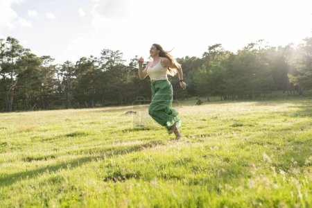 Capturing a moment of pure joy, a young woman runs barefoot through a sun-drenched field, her green skirt and hair flowing in the breeze.