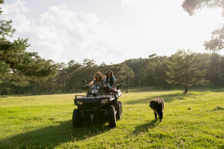 Un paseo alegre en el bosque con amigos y un perro en un ATV, capturando un momento de aventura y compañía bajo el sol.